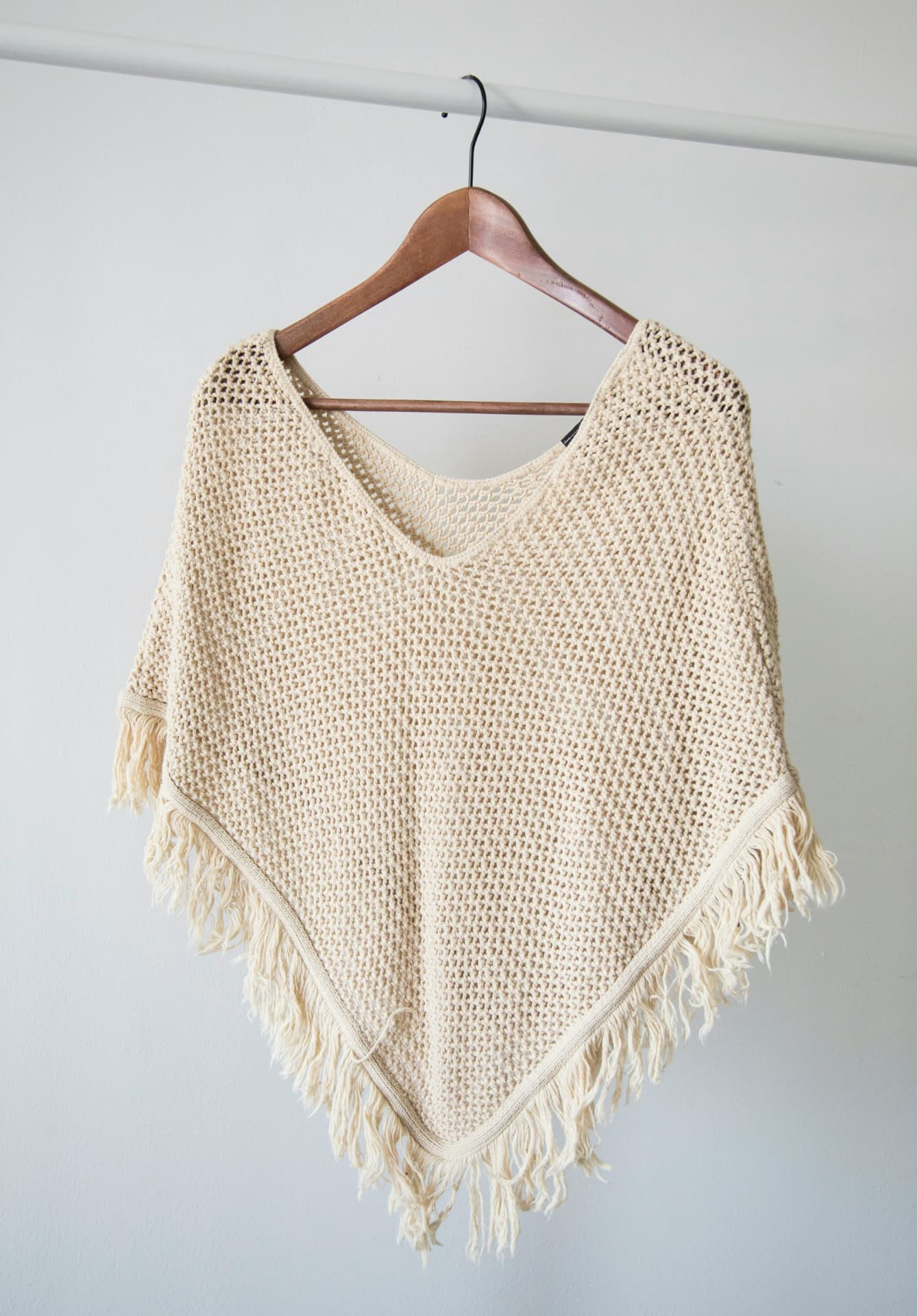 A cream knitted piece on a wooden hanger, prepared for clothing resale